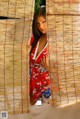 A woman in a red dress standing in front of a bamboo wall.