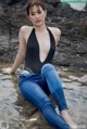 A woman in a black bathing suit sitting on a rock in the water.