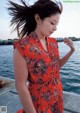 A woman in a red floral dress standing by the water.