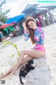 A woman in a bikini sitting on the beach with a cat.