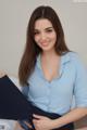 A woman in a blue shirt is sitting on a bed.