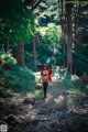 A woman in a red riding hoodie is walking through the woods.