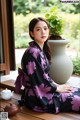 A woman in a black and purple kimono sitting on a wooden floor.