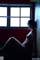 A naked woman sitting in front of a window.