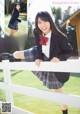 A woman in a school uniform leaning against a fence.