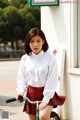 A woman in a white shirt and red plaid skirt riding a bike.