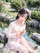 A woman in a pink kimono sitting on a rock by a pond.